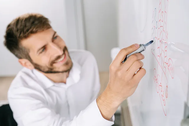 A professional man writing ideas on a whiteboard in a modern office setting. Commercial cleaning scheduling for owners